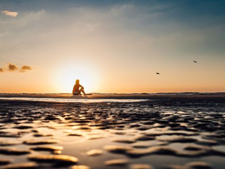 Eine Frau sitzt im Sonnenuntergang im Watt auf der Insel Norderney